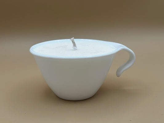 White ceramic teacup candle with a handle on a beige background
