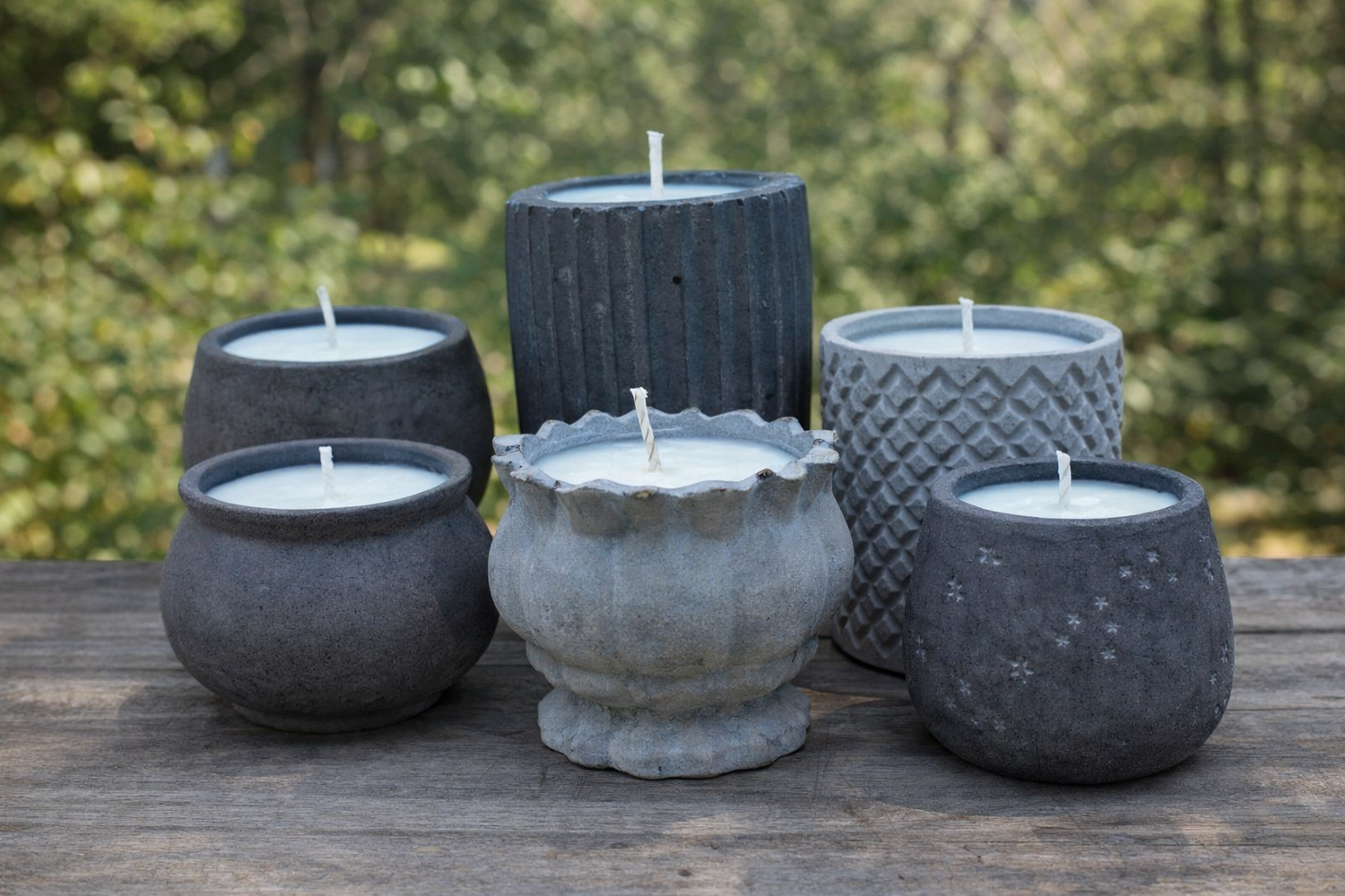 Handmade concrete candle collection from Órale Homestead featuring modern textured stone vessels displayed on a wooden table outdoors.