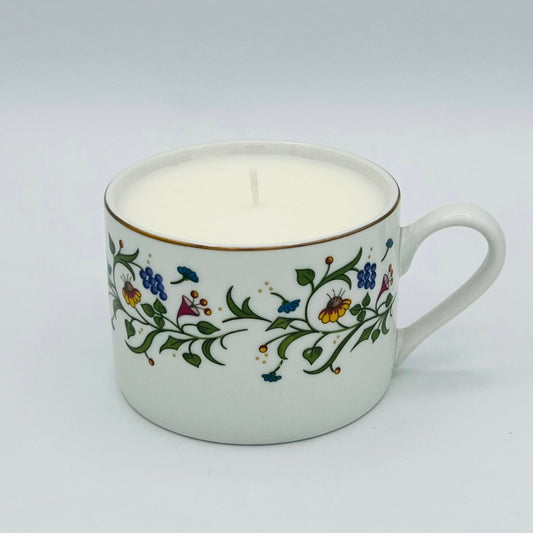 Ceramic mug with floral design containing a lit candle on a white background