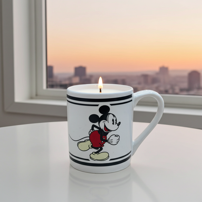 Mug candle with Mickey Mouse design lit from within, placed on a surface with a window view of a cityscape.