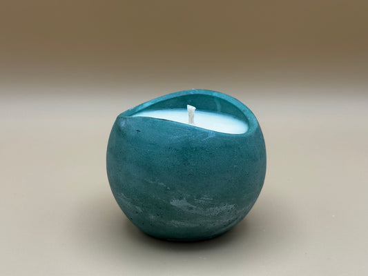 Teal concrete candle holder with a white candle inside on a beige background