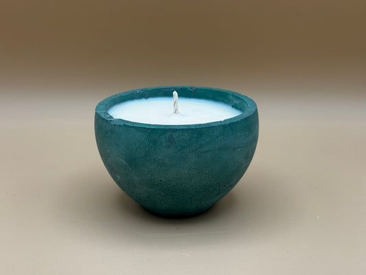 Green concrete candle holder with a white candle inside on a beige background