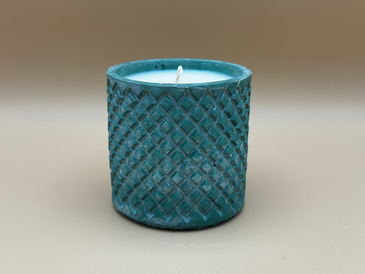 Teal textured candle holder with a white candle inside on a beige background