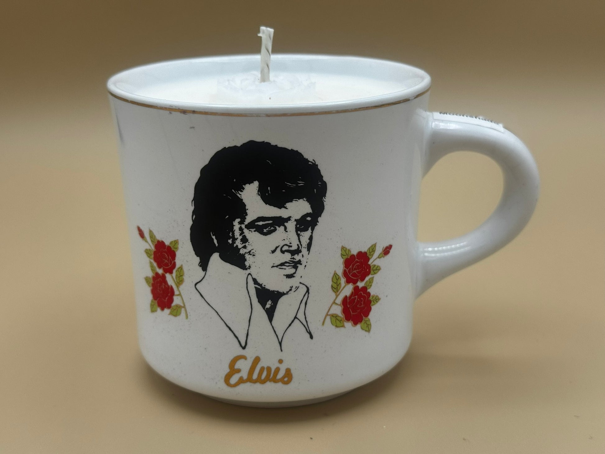 Candle in a mug with a portrait of Elvis Presley and flowers on a beige background