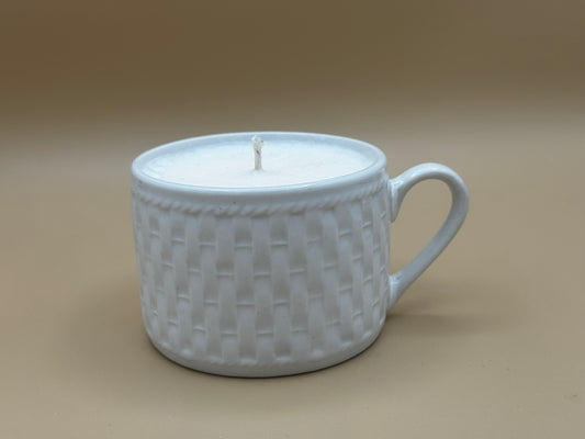 White ceramic mug with woven pattern containing a candle on a beige background